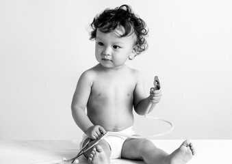 Cute curly haired toddler sitting on exam table before health check-up at hospital and playing with...