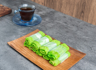 Delicious Indonesian dadar gulung dessert neatly served on a wooden plate with coffee and leaf...