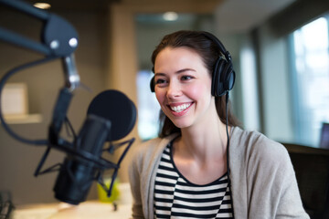 Young adult Caucasian woman co-hosting a podcast from her cubicle, speaking into a mic and smiling confidently