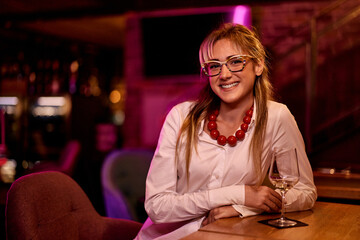 Smiling Woman Relaxing at a Bar With a Glass of White Wine