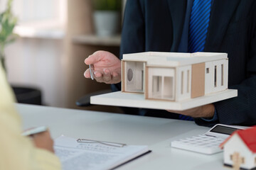 Real estate agent handing over house model to client during consultation