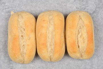 Three baked, oval-shaped rolls are placed on a gray, mottled background, photographed from above