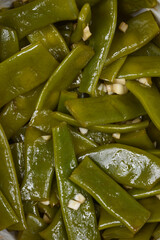 A close-up view shows the texture and details of a cooked green bean and garlic salad, highlighting...