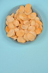 A blue bowl filled with crunchy wheat and oat snacks, placed on a blue background, photographed from above