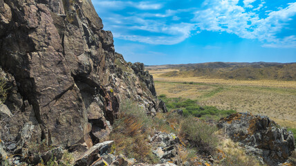 A scenic image shows a rocky cliff on one side and a sunny valley with yellow grass on the other, evoking a peaceful desert landscape.