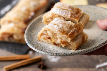 hand holding a plate with some slices of apple strudel