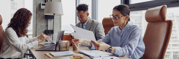 A diverse and talented team is engaged in a collaborative office meeting filled with important documents and laptops