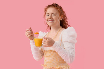 Young redhead woman with turmeric drink on pink background