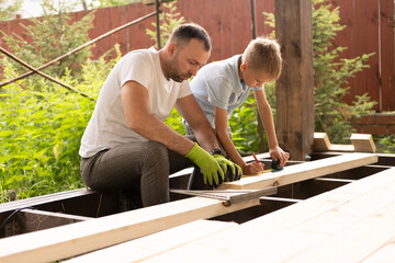 A father and his young son are building wooden house, making markings. The concept of carpentry and family.