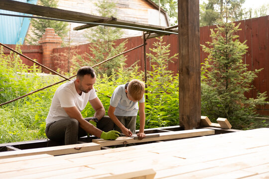 A father and his young son are building wooden house, making markings. The concept of carpentry and family.