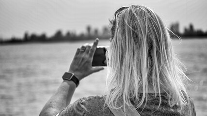 Woman photographing New York City skyline with smartphone from Liberty Island
