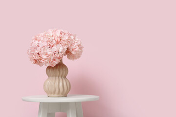 Vase with hydrangea flowers on table near pink wall