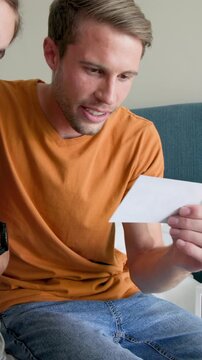 Vertical video: Expectant couple opening card, sharing pregnancy news and touching belly in bedroom