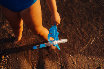 Child walking on the beach holding snorkeling gear