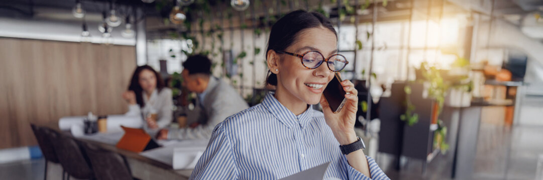 A cheerful and smiling professional engaged in a phone call within a contemporary office environment