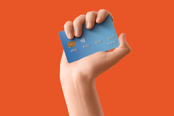 Female hand with credit card on orange background, closeup