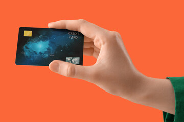 Female hand with credit card on orange background, closeup