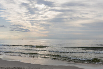 Waves washing sandy beach at sunset with cloudy sky. Sea horizon and evening light. 