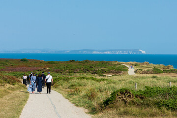 Hengistbury Head, Southbourne, UK - August 10th 2025: Group of people walking on the footpath on Warren Hill with the Isle of Wight in the background.