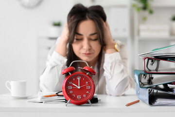 Alarm clock on table against stressed businesswoman in office, closeup. Time management concept