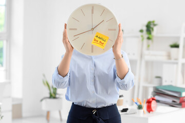 Businesswoman holding clock with text MANAGE YOUR TIME in office