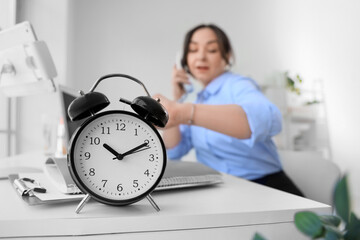 Alarm clock on table against businesswoman talking by phone in office, closeup. Time management...