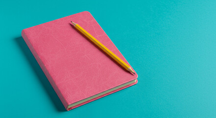 Fototapeta premium A pink notebook with a yellow pencil lying diagonally across it on a blue background flat lay