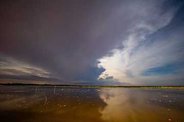 Time lapse Lightning over the lake Nature balances chaos and serenity as a massive storm cloud towers above, its edges glowing faintly with filtered sunlight. Below, the lake remains perfectly still
