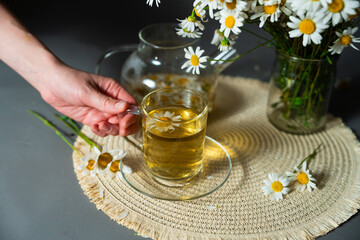 Chamomile bouquet and cup of herbal tea create cozy atmosphere. Scented mood reflects harmony,...
