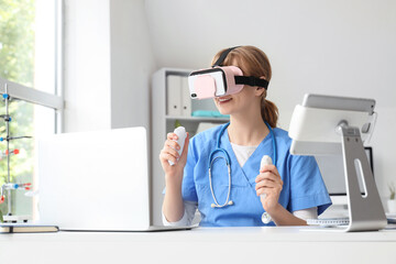 Female doctor using VR glasses with controllers at table in clinic © Pixel-Shot