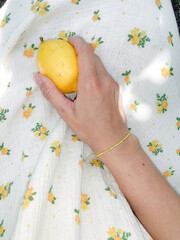 Hand holding lemon on floral summer dress
A hand with a delicate bracelet holding a fresh yellow...