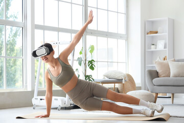 Sporty young woman in VR glasses exercising on yoga mat at home
