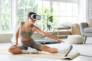 Sporty young woman in VR glasses exercising on yoga mat at home