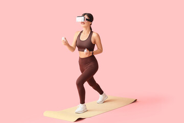 Sporty young woman in VR glasses exercising with controllers on pink background