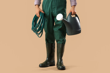 Male gardener with watering can and hose on beige background