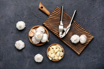 Bowls and wooden board with fresh garlics on dark background