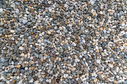 Mixed natural pebbles forming stone surface. Top view of assorted natural pebbles in various colors and shapes, perfect for texture backgrounds or outdoor design concepts.