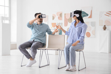 Young couple with VR glasses talking on chairs in modern art gallery