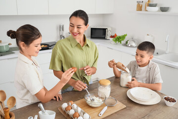 Young mother with her children preparing dough in kitchen