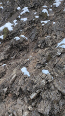 Rocky cliff covered with small patches of snow. Detail of rugged mountain surface in winter.