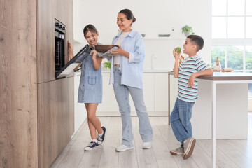 Young mother with her children putting apple pie into oven in kitchen