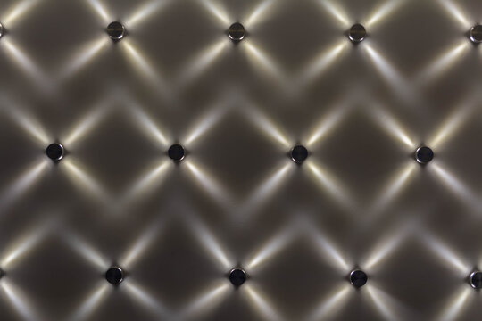 A close-up of small LED lights mounted on a wall, creating an abstract, repeating geometric pattern with crisscrossing beams of light.
