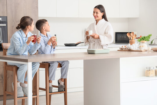 Young mother with her children drinking juice and coffee in kitchen