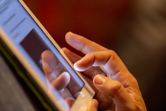 A person's hand is shown in a close-up, gently touching the glowing screen of a digital tablet. The shot represents modern technology and digital connection.
