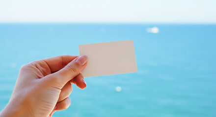 Blank hotel key card held against a clear ocean backdrop on a sunny day by the coast