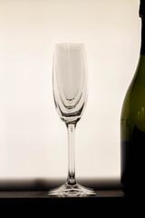 An empty, elegant champagne glass stands beside a bottle, with a clean and bright white background. A symbol of upcoming celebration.