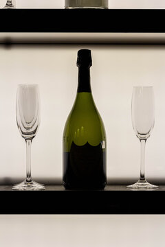 A bottle of champagne flanked by two empty flutes on a black shelf, set against a glowing white background. The image represents a celebration.