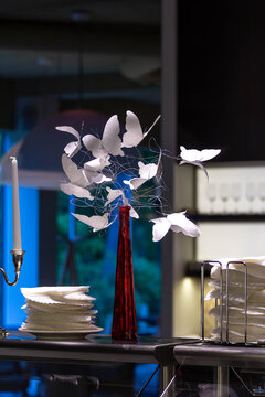 A close-up of a stylish restaurant table with a creative centerpiece of white paper butterflies and a single candle. The shot represents elegant decor and atmosphere.