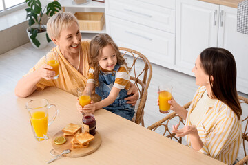 Little girl with her mother and granny drinking juice at table in kitchen