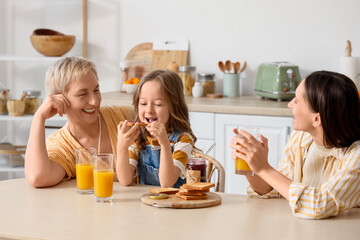 Little girl eating toast with her mother and granny in kitchen